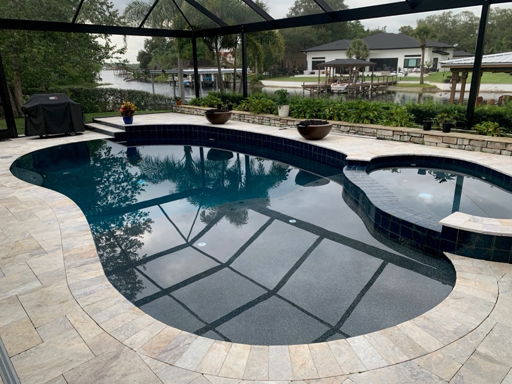 Lakefront pool resurfaced to dark water with travertine deck and fire bowls
