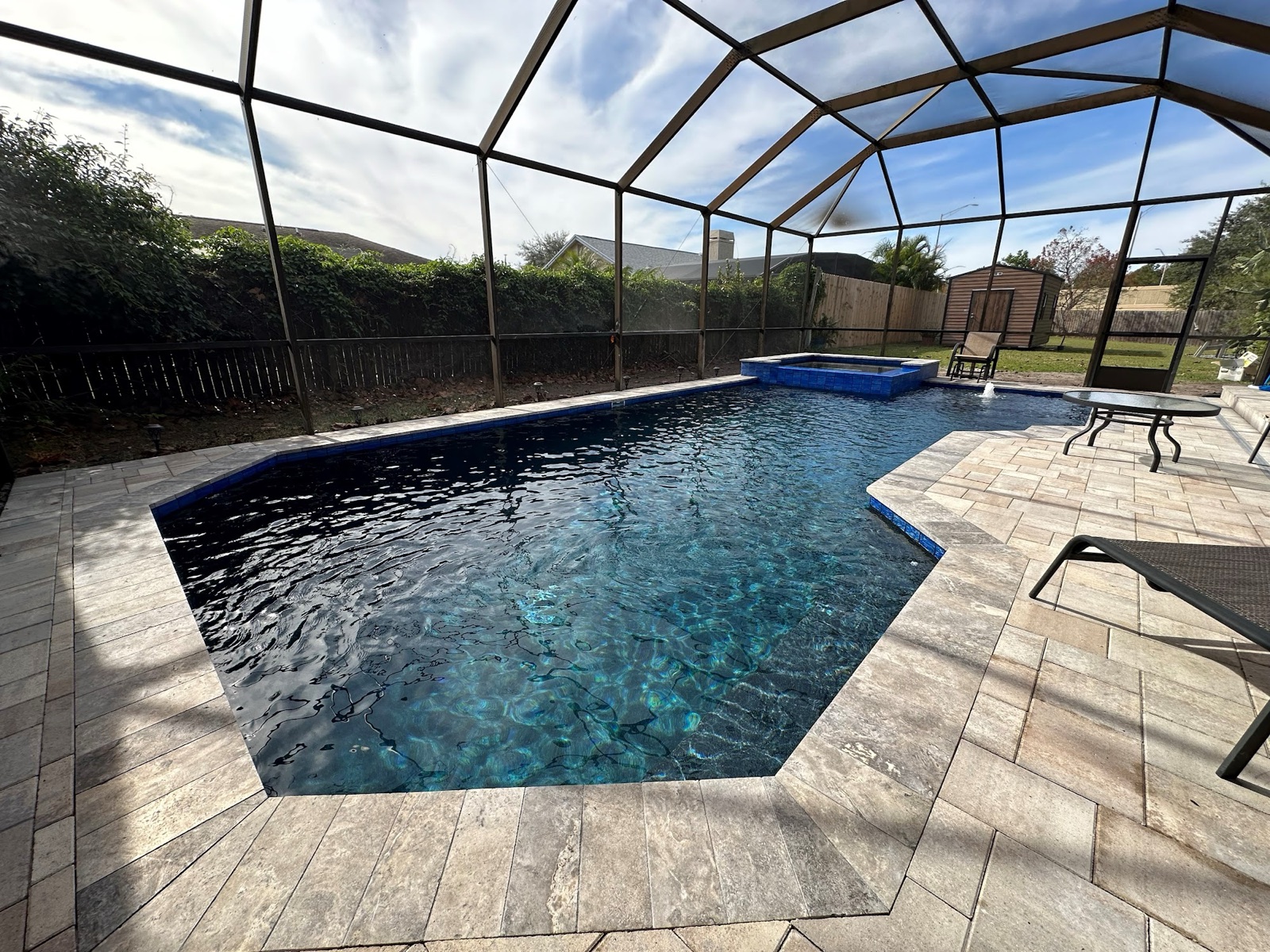 Screen-enclosed pool with deep blue water and travertine deck