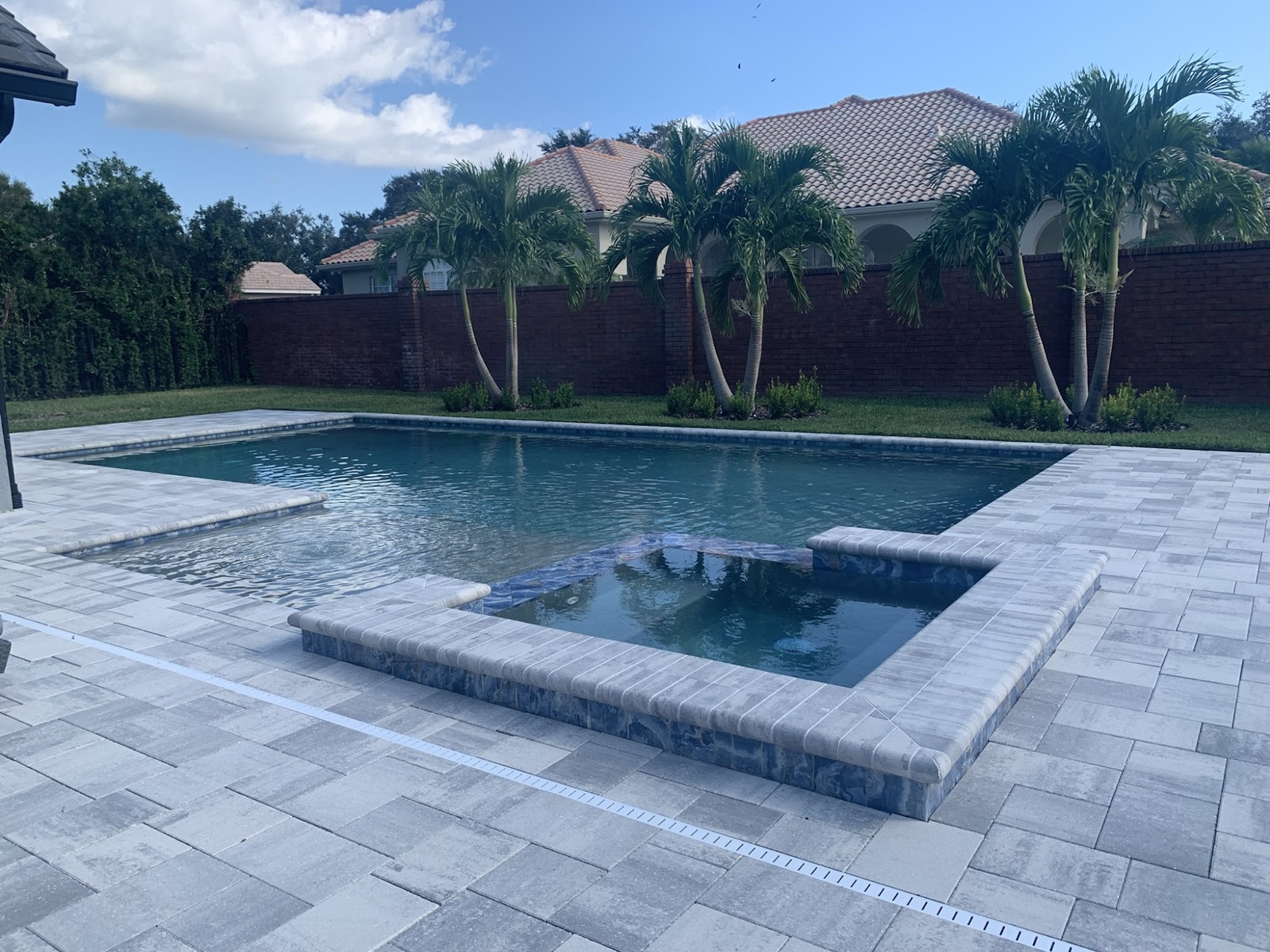 Pool corner with water-feature scuppers and in-deck white loungers under screen enclosure
